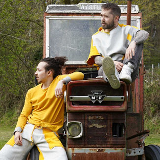 Tractor Time! MCDC. Two young light-skinned men rest on a tractor hood, looking into the distance