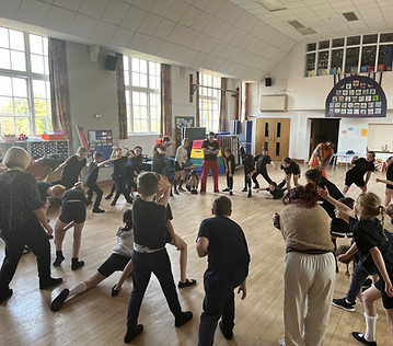 Mo leads a big group of children in a school hall, all performing exaggerated gestures