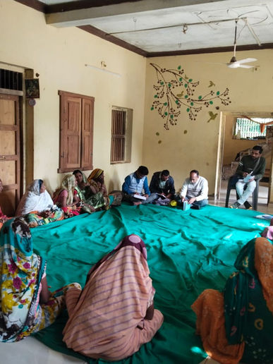 Group of people seated on a green cloth, meeting indoors