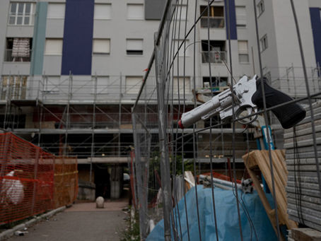 Una pistola a salve incastrata in una rete con, sullo sfondo, dei palazzi ristrutturati a Tor Bella Monaca