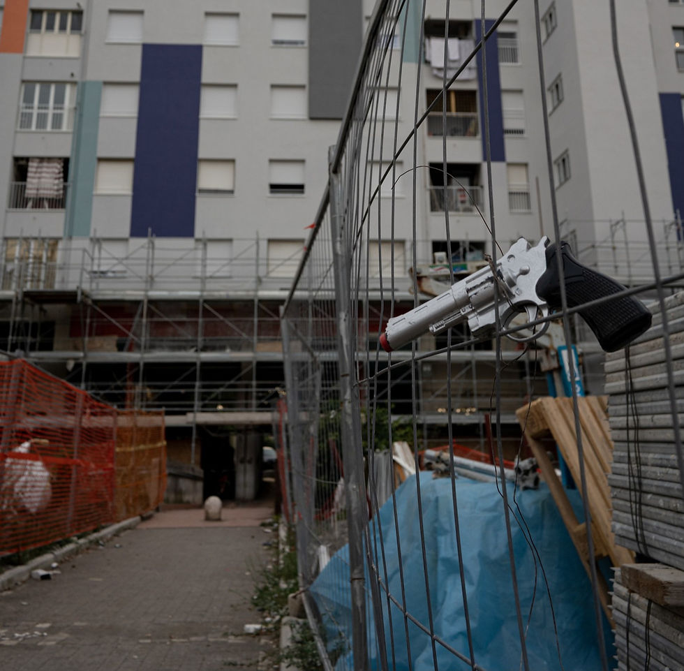 Una pistola a salve incastrata in una rete con, sullo sfondo, dei palazzi ristrutturati a Tor Bella Monaca