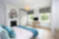 An example of a loft conversion for a Barnet property showing a large converted bedroom conversions showing two sash windows, a wooden desk, fireplace and large double bed.