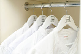 White clothes hangers with Chefs Wardrobe logo and chef jackets hanging on a rail