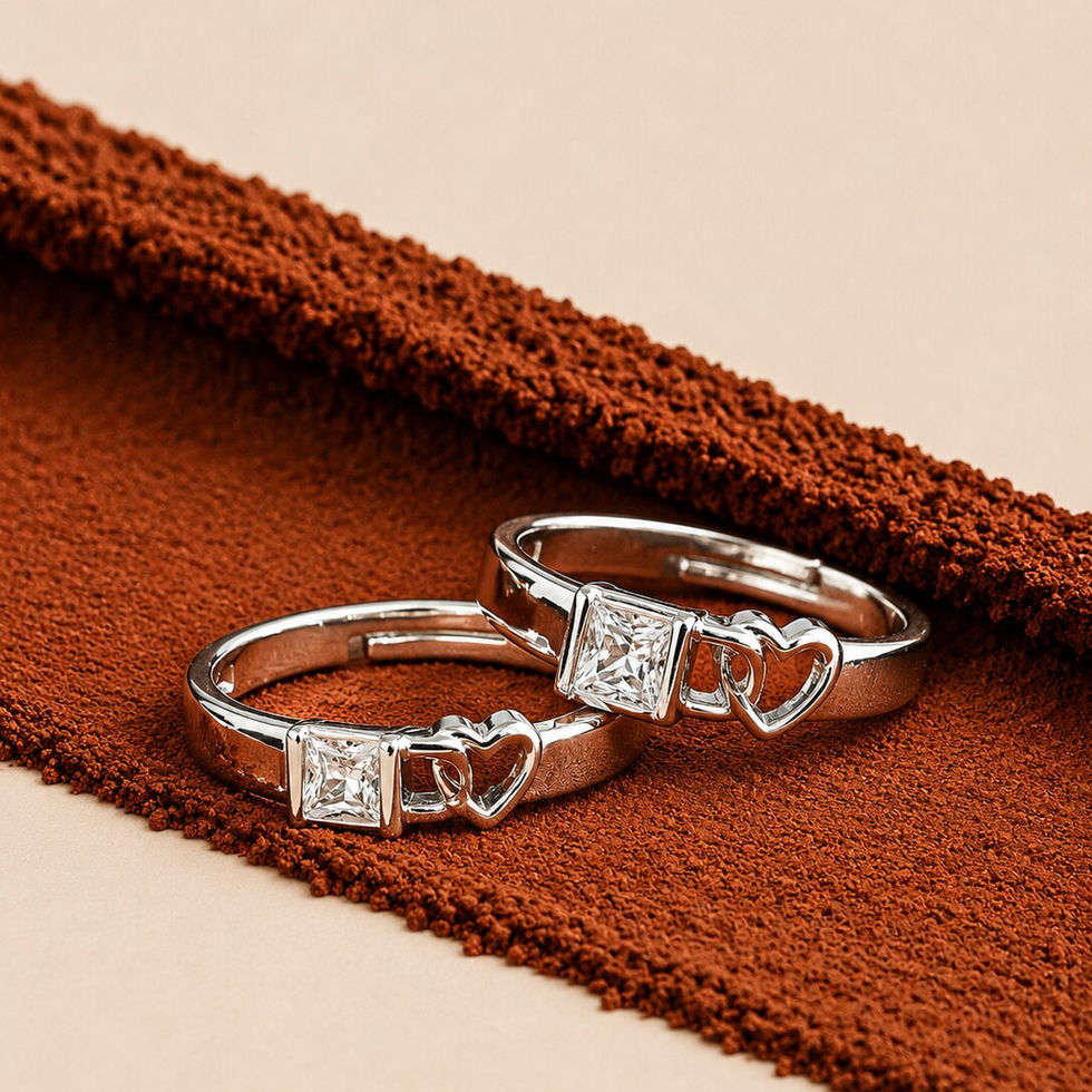 Silver couple rings with square crystal stones and heart detailing placed on a textured brown surface.