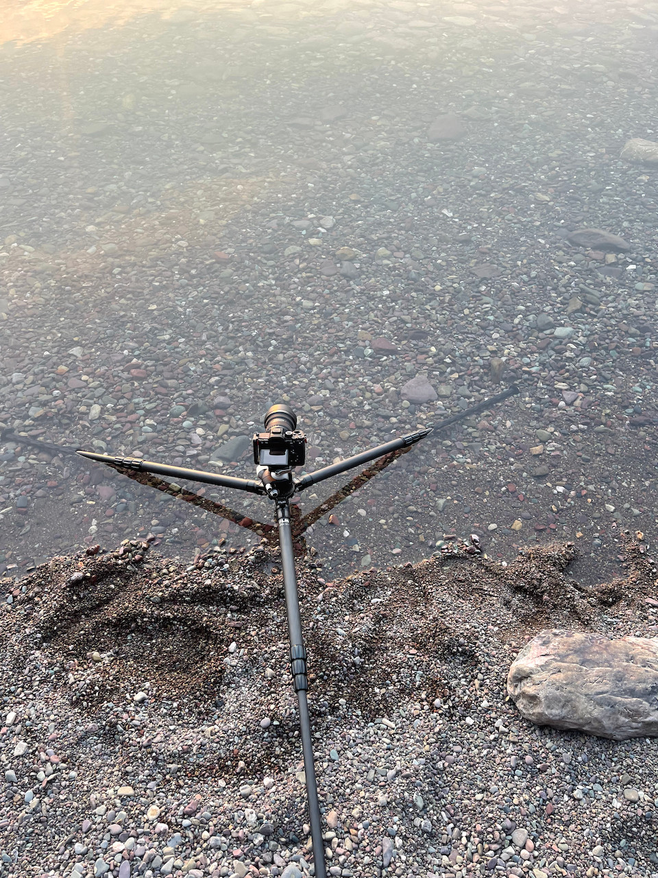 A camera mounted on a tripod on the lakeshore - the legs of the tripod are spread wide so the camera can be low slung and perfectly capture the water's surface