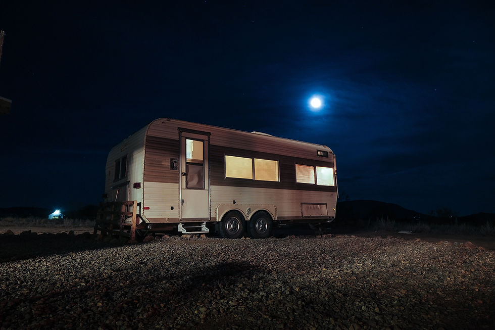 The moon shines brightly over an older RV trailer, parked in the middle of the desert at Joshua Tree National Park