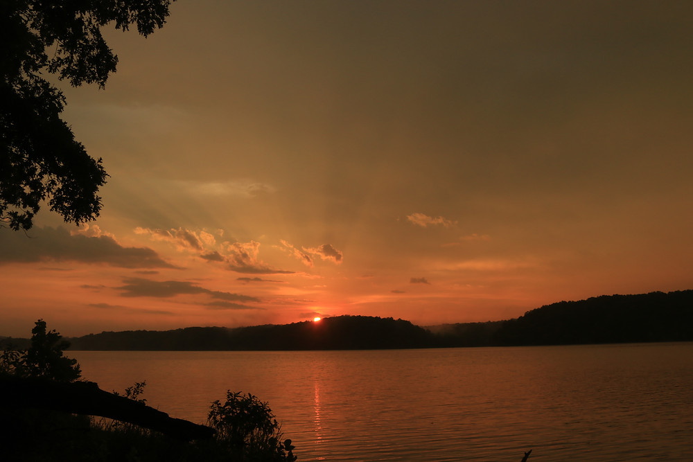 Sunset over the beautiful lakes of southern Alabama. The sky is lit up with oranges over a wide lake, with hills on the opposite coast in the background
