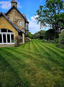 Freshly mowed striped lawn next to a stone house, maintained by Alba Hybrid Contractors in Fife.