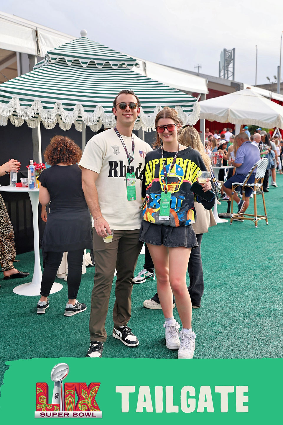 Two fans smile under striped canopies during the Super Bowl LIX Tailgate in New Orleans, celebrating with drinks and branded experiences.