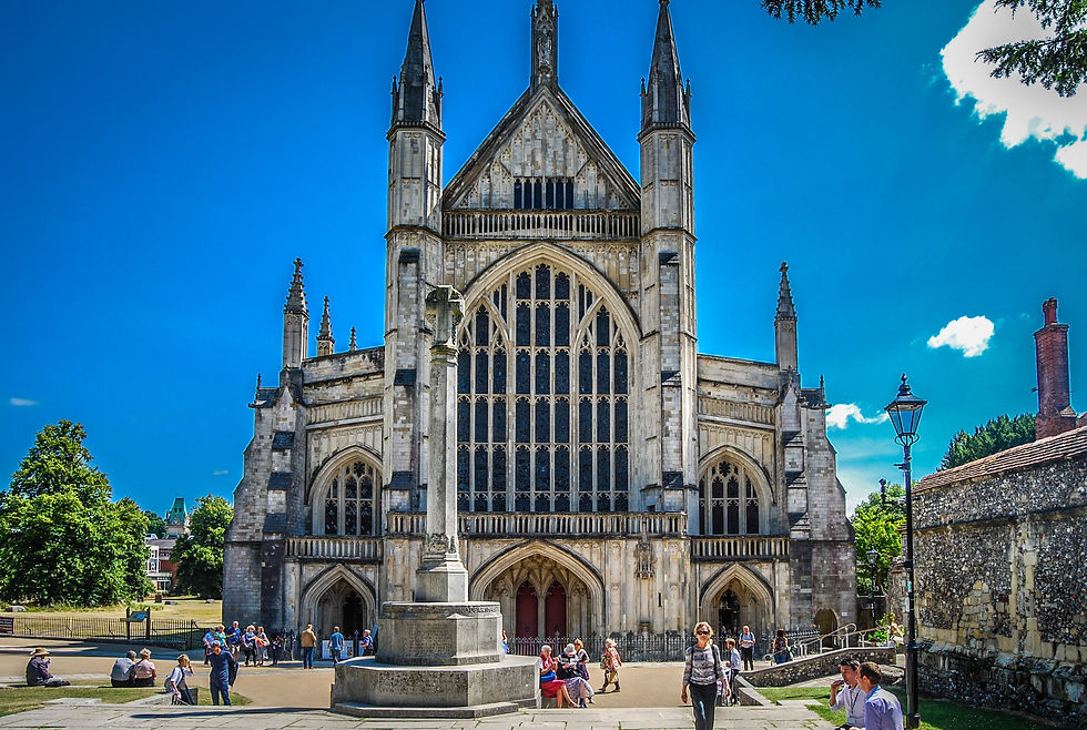 People gather outside Winchester Cathedral under a bright blue sky.