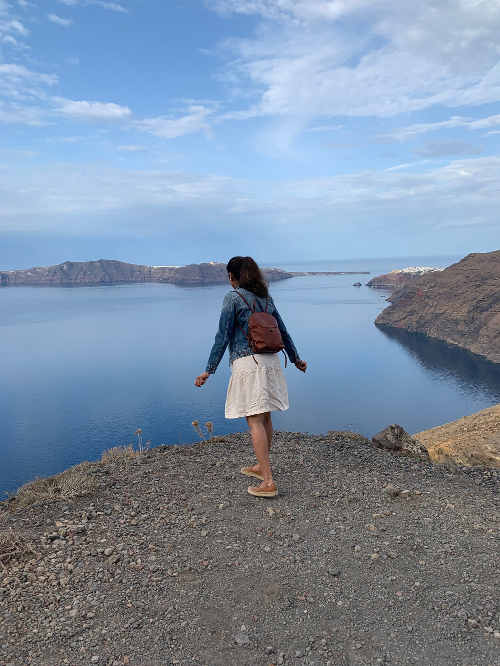 Vaishali Patel of Sanskar Teaching looking over the edge of a steep cliff on the path between Oia and Fira in Santorini Greece