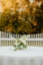 White wedding and event florals on a table by a fence.