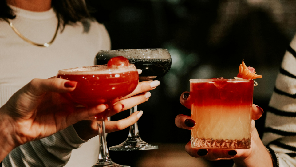 Three female colleagues' hands holding different Christmas cocktails.