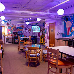 Community room with tables, chairs, colorful mural, and ambient lighting, rental space.
