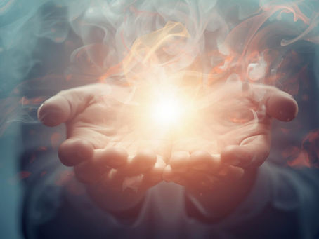 Hands cupped together hold glowing light with swirling smoke, creating a mystical aura. Background is blurred with blue and orange hues.