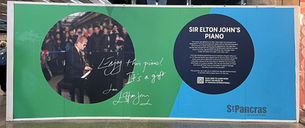 A display at St. Pancras International showing Sir Elton John playing the Yamaha piano he donated to the station in 2016. The wall includes his handwritten message: "Enjoy this piano! It’s a gift. Love, Elton John," alongside information about the piano’s legacy and a QR code linking to past performances.
