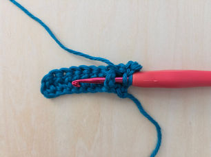 Crochet hook inserted around the post of a teal Double Crochet Stitch.