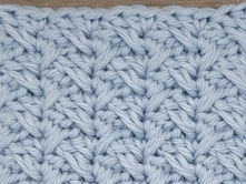 Close-up of light blue yarn crocheted in the Spiked Sedge stitch, showing elongated Double Crochet stitches crossing between grouped shorter stitches.