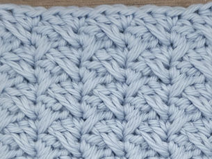 Close-up of light blue yarn crocheted in the Spiked Sedge stitch, showing elongated Double Crochet stitches crossing between grouped shorter stitches.