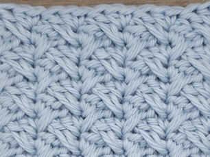 Close-up of light blue yarn crocheted in the Spiked Sedge stitch, showing elongated Double Crochet stitches crossing between grouped shorter stitches.