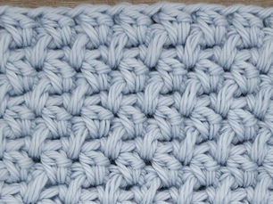 Close-up of light blue yarn crocheted in the Bamboo stitch, showing compact paired stitch groups separated by chain one spaces.