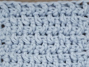 Close-up of light blue yarn crocheted in the Rice stitch, showing raised alternating Front Post and Back Post Double Crochet stitches.
