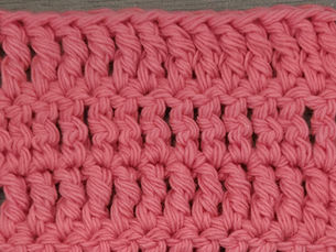 Close-up of pink yarn worked in rows of Treble Crochet stitches.