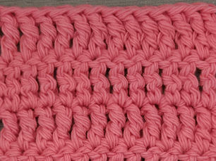 Close-up of pink yarn worked in rows of Treble Crochet stitches.