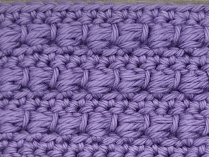 Close-up of purple yarn crocheted in the Bead stitch, showing raised wrapped stitch clusters arranged in horizontal rows.