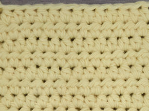Close-up of yellow yarn worked in rows of Half Double Crochet stitches.