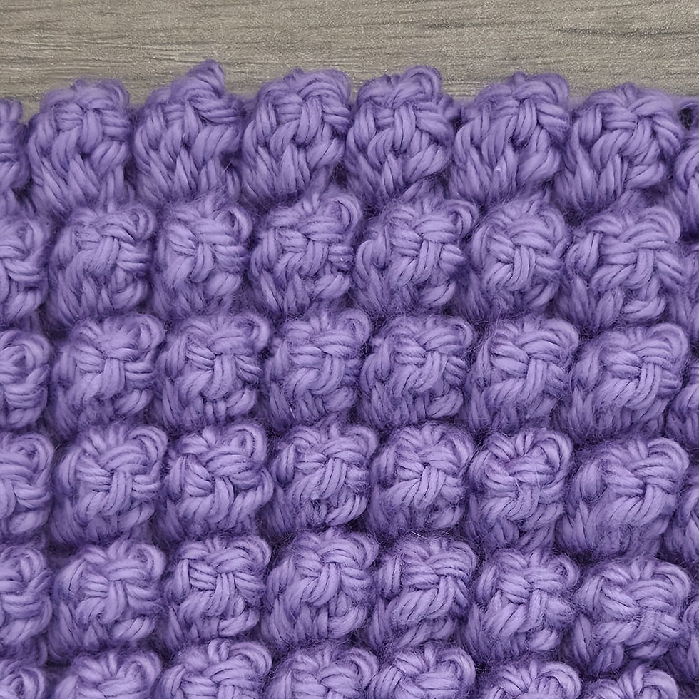 Close-up of purple yarn crocheted in the Popcorn stitch, showing rows of prominent rounded five Double Crochet popcorns.