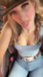 Blonde woman wearing a hat and jeans, tongue slightly out