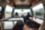 Cozy camper van interior with a bed, table, and cabinets. Large windows reveal a serene mountain view. Relaxed, inviting atmosphere. follow the nomadic life, get advice and tips by reading blog.