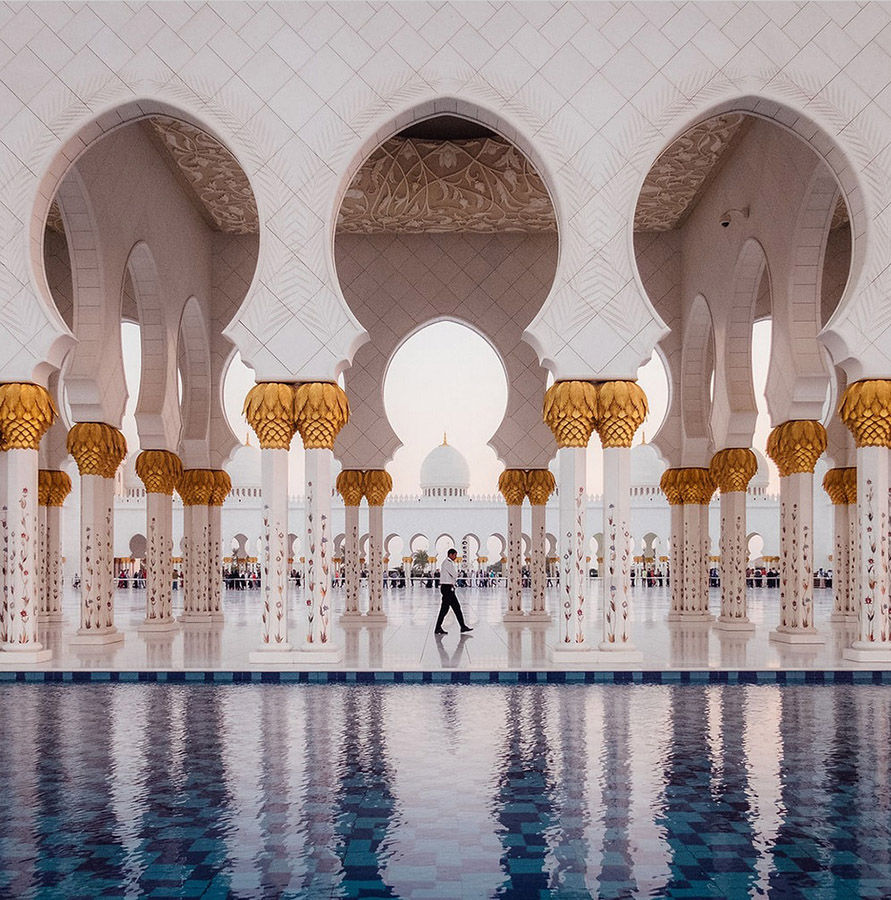 White marble columns with gold accents and Arabic arches framing the inner yard of the Sheikh Zayed Grand Mosque in Abu Dhabi