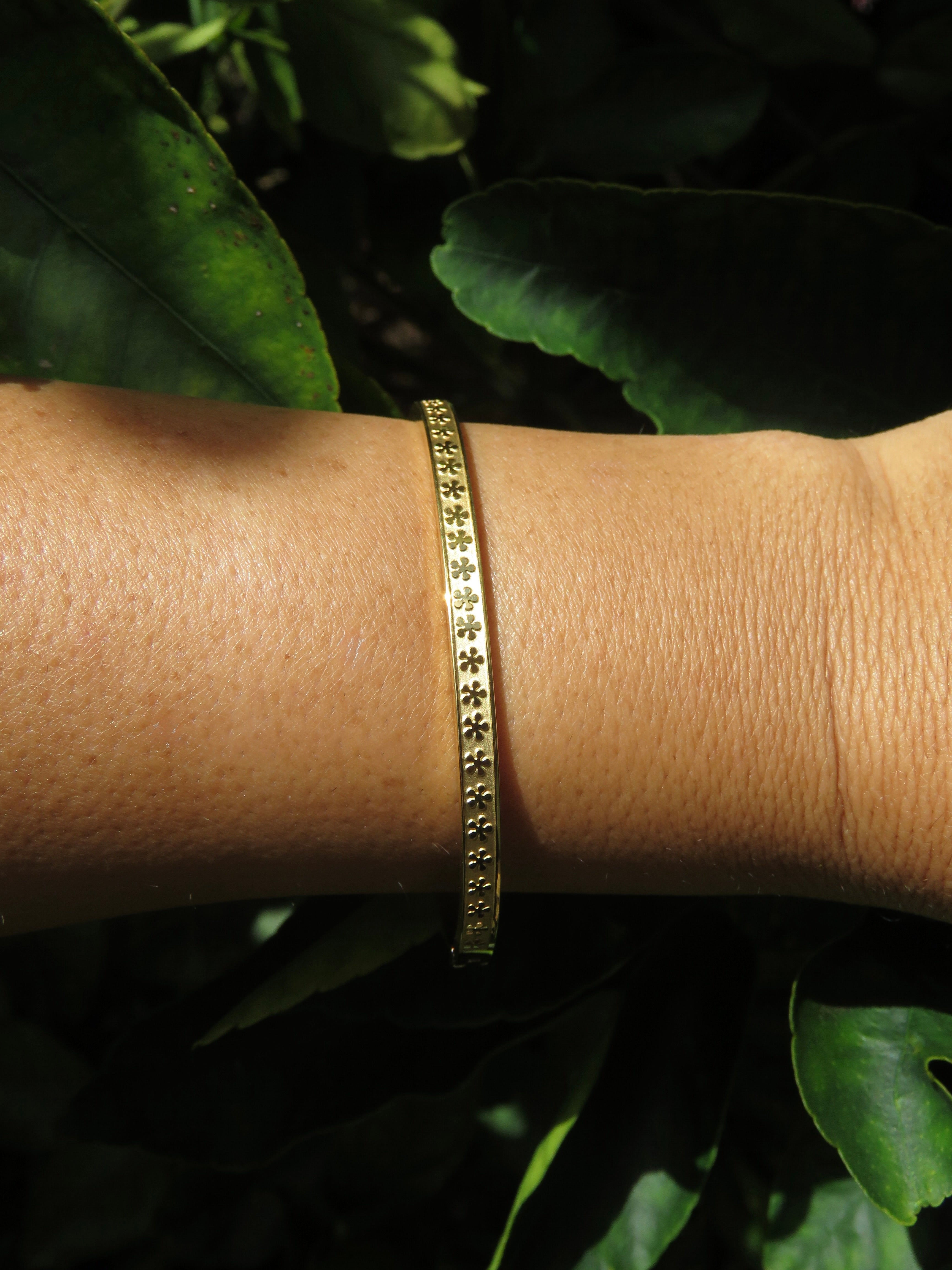 Gold bangle bracelet with flowers with five petals displayed on a green leafy background