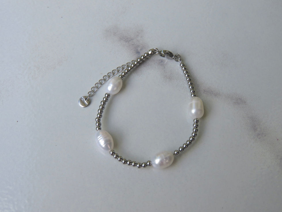 Silver beaded bracelet with white fresh water pearls on it displayed on a white background