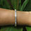 Thumbnail: Gold bangle bracelet with rectangular cubic zirconia stones displayed on a green leafy background