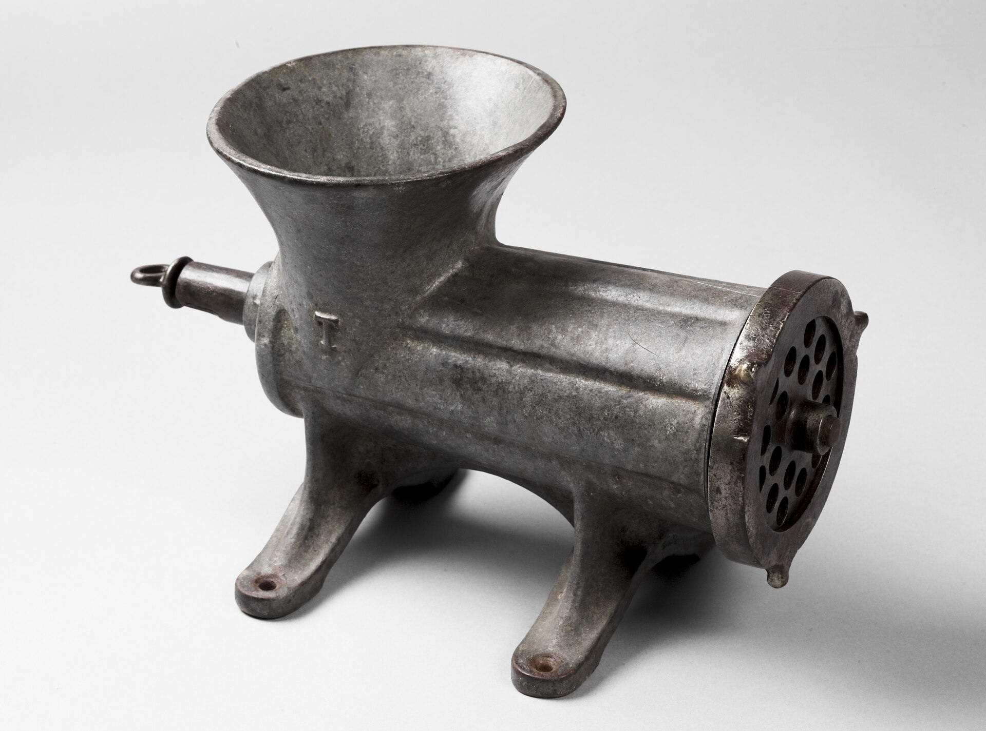 Historischer Tischfleischwolf aus Gusseisen und Eisen auf vier Füßen, aufbewahrt in den Musei del cibo; die Kurbel fehlt.