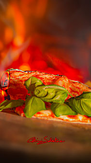 Pizza artisanale posée sur les braises d’un four à bois à La Corte Segreta, basilic frais vibrant sur fond de chaleur rougeoyante, osteria italienne à Casteau près de Soignies, Maisières, Lens et Mons, symbole de renaissance, résilience et mémoire sicilienne