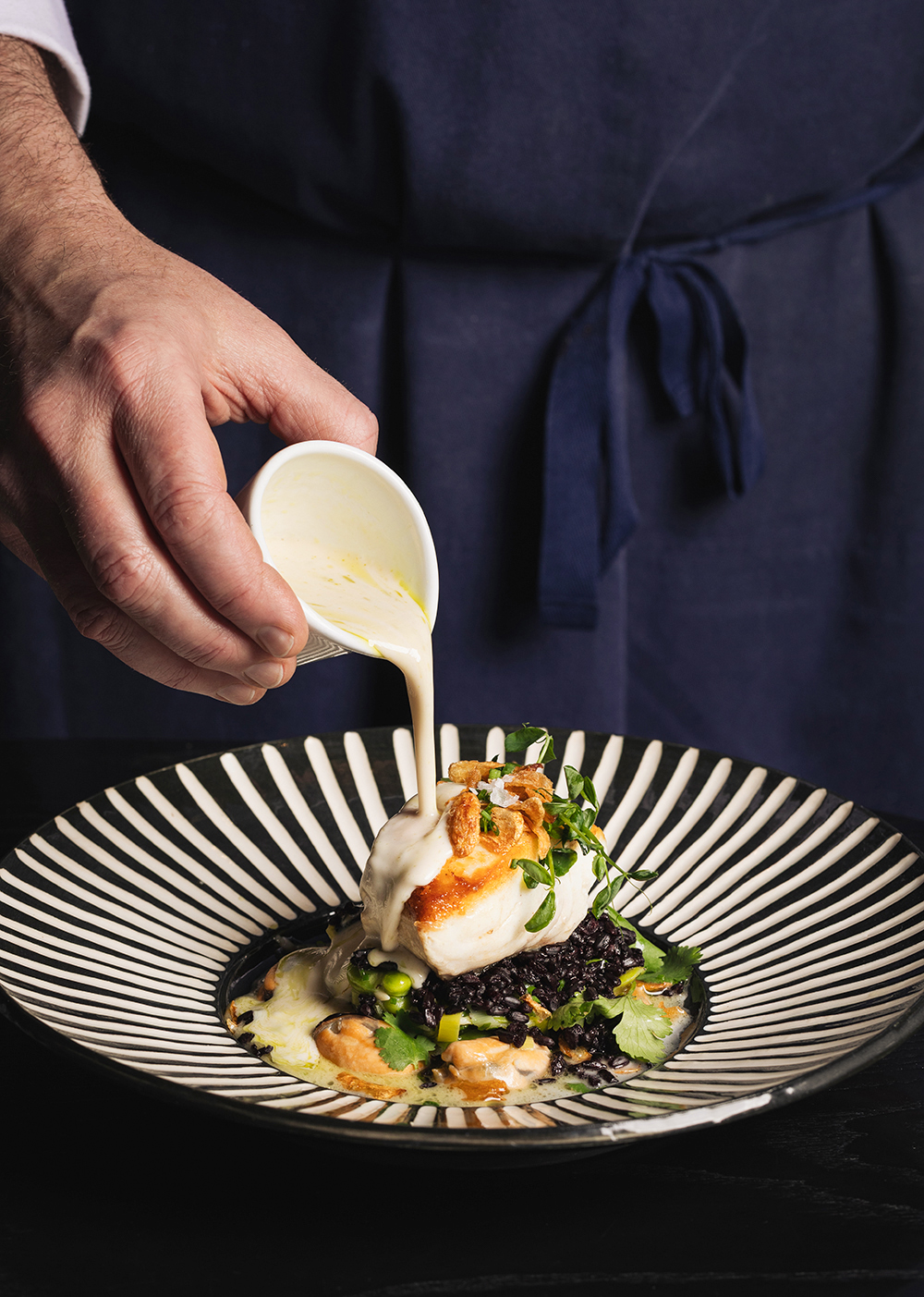 “Chef plating dessert with sauce on a patterned plate, close-up.”
