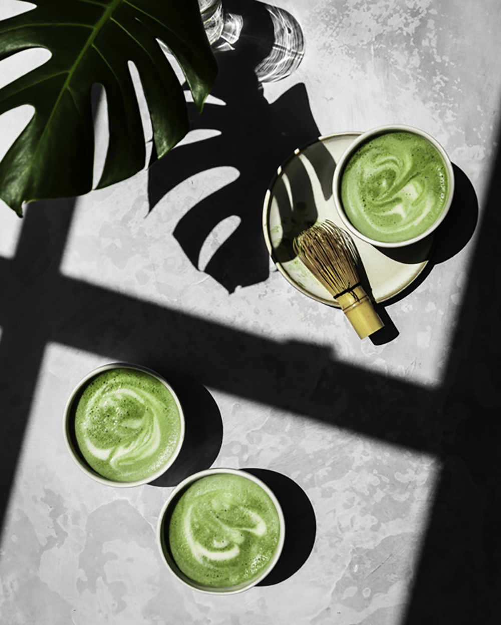 Matcha lattes on a table with leaf shadow