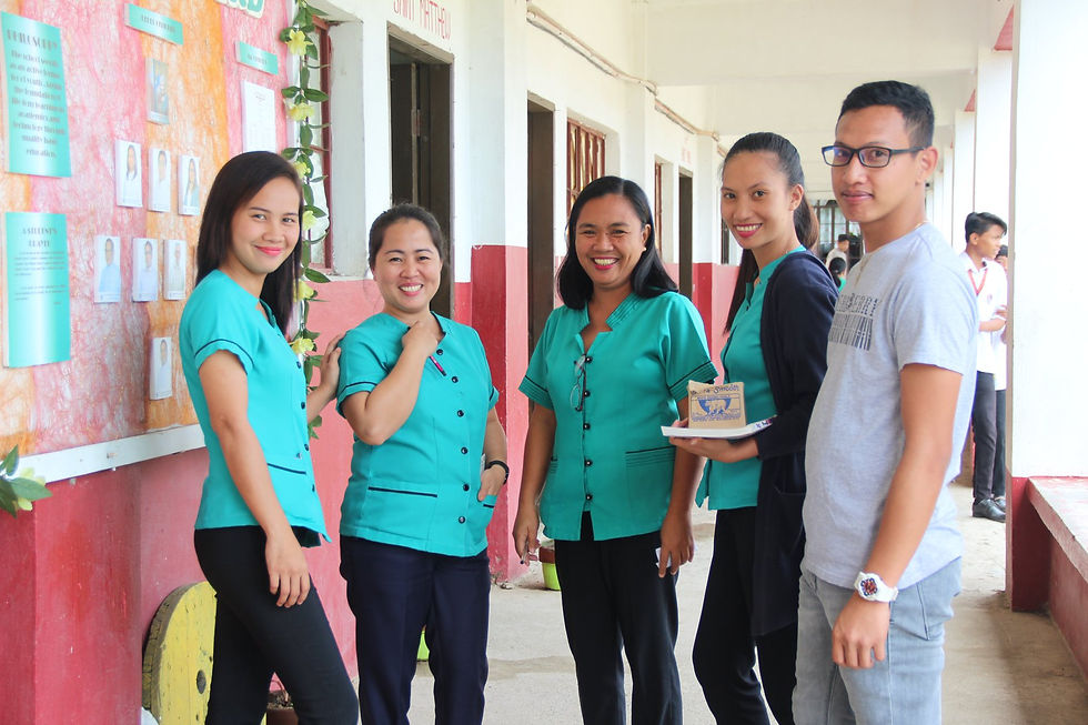 Five people smile in a school hallway. Four wear teal uniforms; one holds an award. A colorful bulletin board is visible in the background.