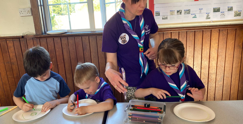 An adult shows a Beaver Scout an image on her phone while they create images on paper plates