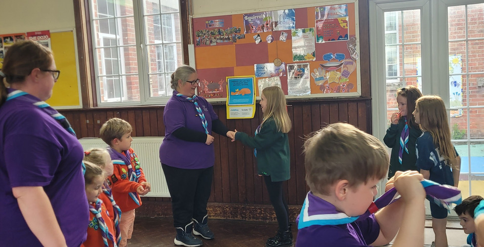 A former Beaver Scout is awarded a badge by an adult while the rest of the group watches