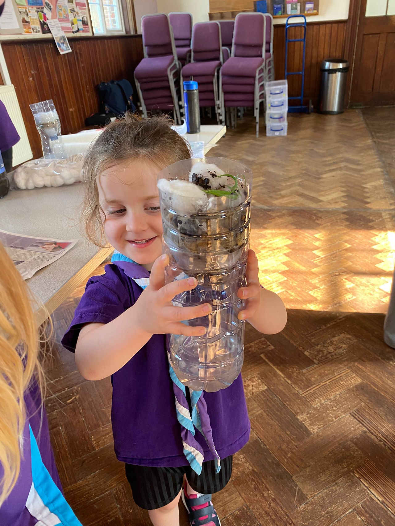 A Squirrel Scout holds up her water filter to show the results. The bottom contains slightly cloudy water