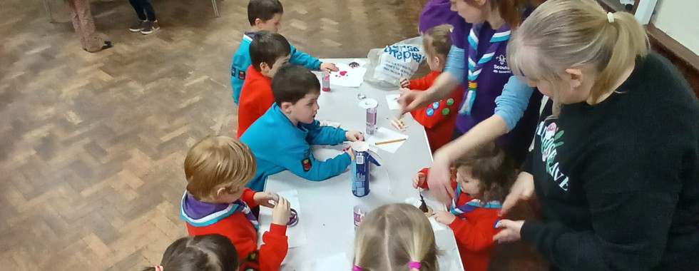 Beaver and Squirrel Scouts gather around a table with some leaders to decorate biscuits