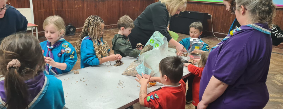 Beaver and Squirrel Scouts sit around a table with their leaders to make bird feeders