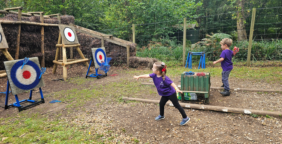 Two Squirrel Scouts throw plastic tomahawks at a plastic and foam target