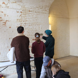 Three adults stand at a table while two others are sat at the floor behind them