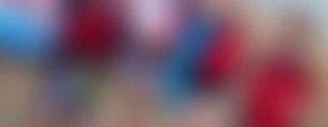 Two Squirrel and two Beaver Scouts in water wear and life vests stand on the shore next to some boards, an adult stood behind them